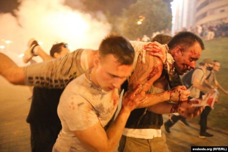 Two men carrying a heavily hurt man with blood dripping everywhere. Picture taken during a protest in Minsk against Lukashenko and his regime.